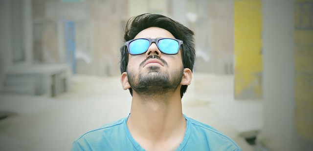Muž v modrom tričku a slnečných okuliaroch s modrými sklami pozerá smerom nahor